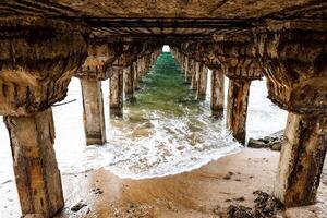 Waves under the pier. Beautiful bright green water with clean foam under the pier. A shot with perspective. Old beautiful pillars hold the pier. photo