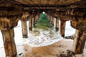 olas debajo el muelle. hermosa brillante verde agua con limpiar espuma debajo el muelle. un Disparo con perspectiva. antiguo hermosa pilares sostener el muelle. foto