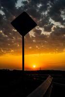 Breathtaking view of the sunset on the track. The road goes into the distance, the Shadow of the road sign. Incredibly beautiful sunset bright scarlet color and cumulus clouds in the sky. photo