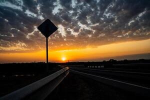 Incredibly beautiful sunset in the countryside. Bright peach and orange sunset and cumulus clouds in the sky. Sunset on the highway, the shadow of the road sign.. A road that goes into the distance. photo