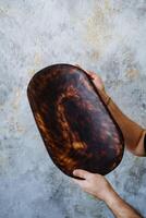 Tableware made of natural and high-quality material, wooden kitchen utensils. In his hands, a person holds a large oval plate with an unusual pattern. photo