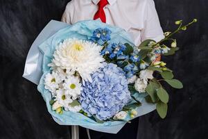 A boy with a red tie has a large festive bouquet of white and blue flowers. The bouquet is collected for the first of September. photo