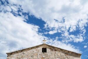 el parte superior de el Iglesia con un cruzar en contra un brillante azul cielo. parte de el templo es hecho de blanco Roca. minimalista marco de arquitectura. puro colores foto