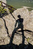 The human shadow is visible on the rock on a very sunny day. Small green bushes grow on the stones and part of the iron staircase is visible. photo