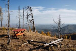 A picnic table stands on top of a mountain, a great place to relax, there are trees without foliage nearby. The onset of autumn in the mountains, active recreation in the mountains photo