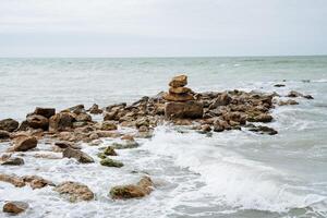 Sea surf. The waves beat against rocks and stones. A hill of stones, a rocky shore in the sea. The beauty of the sea wave, thick foam. photo