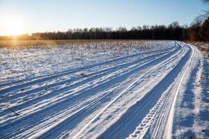 Winter time. A winding road through a snow-covered field goes far ahead. Ice-bound winter forest ahead photo