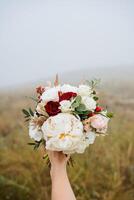 el novia con un Delgado y elegante mano sostiene un Boda ramo de flores de delicado blanco y rojo flores foto