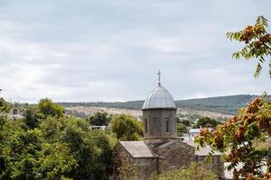 Ancient single-domed temple. Historical building in the middle of the landscape. Church and service, cross on the dome. Around the temple there are green trees photo