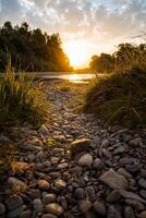Incredibly beautiful sunset by the river. Rocky shore, trail leading to water. In the water surface reflected the sun's rays. Outdoor activities in summer, hiking to the river photo