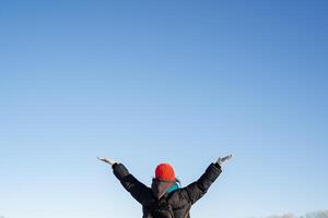 The happy girl raised her hands high to the sky. Delight and joy from the winter landscape with bright sun, clear sky. Walk in nature. photo