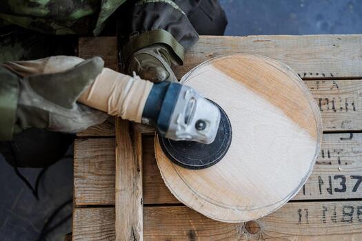 The process of creating utensils from wood. The master cuts a circle of wood, a frame from above. On the hands of special gloves and uniform camouflage print. Wood processing and creation of toys photo