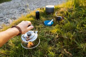 Kettle of silver color to hold in your hand against the background of nature. Tourist breakfast. Cooking in camping conditions. photo