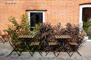 Street terrace of the coffee shop. Wooden tables for two next to the coffee shop behind green bushes. Coffee shop in the city center. photo