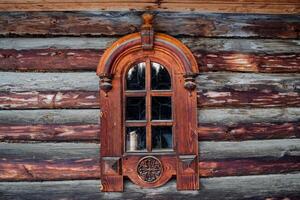 Old wooden window with beautiful carved platbands. Wooden architecture. A small window in the house made of logs. Rustic style photo