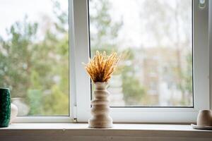 A vase of abstract shape stands in the middle of a light window sill in the workshop. Bouquet of yellow dried flowers in a vase. photo