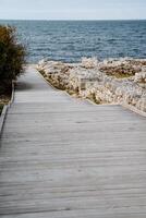 Descent to the sea. Wooden decking going straight to the bright sea. Rocky shore and noisy surf. Walk by the sea. Rest. photo