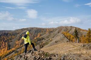 A guy in bright sportswear walks along the top of the mountain, looks forward at the mountains and forest, clear sky overhead, autumn landscape photo