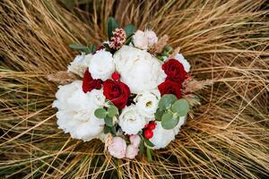 A lush wedding bouquet of white and red flowers lies in the scenery. photo