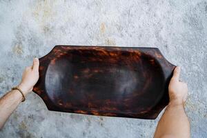 Kitchen utensils made of natural material. In the hands of a man a large wooden tray of dark color. Tableware made by a master of wood carving. photo