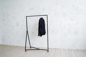 Metal hanger floor on a minimalist background. Rack for clothes on wheels. A black shirt hangs from the hanger. Light walls, wooden floor in the room. photo