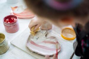un niña pinturas un plato de arcilla en el forma de un rosado unicornio. creatividad en el cerámica taller. foto