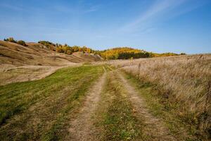 A narrow path, trodden by tourists, going along a mountain range. Bright blue sky overhead, breathtaking view of wildlife, golden autumn forest photo