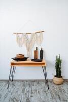 Scandinavian nierier in a minimalist style. a wooden table on elegant legs next to it is a cactus in a pot. the panel hangs on a white wall. photo