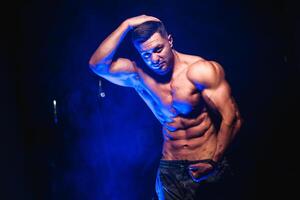 Bodybuilder showing belly and biceps muscles, personal fitness trainer. Strong man flexing muscles. Fitness model posing at camera. Black and blue light background. photo