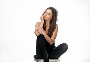 Beautiful long-haired brunette in dark tights sits on the chair in the studio. Attractive woman model in black bodystocking with long hair posing on white background. photo