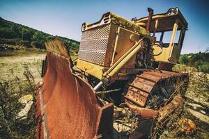 An abandoned old tractor with a bucket on a stone quarry. Old tractor in the field photo