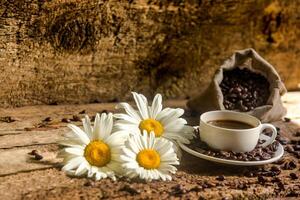 café taza y frito café frijoles en un de madera mesa con hermosa blanco flores en un madera antecedentes foto