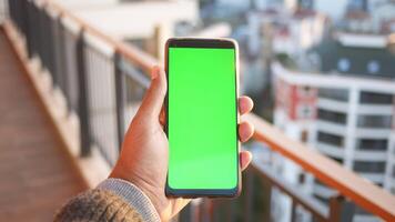 mão de jovem usando telefone inteligente com tela verde contra edifícios da cidade video