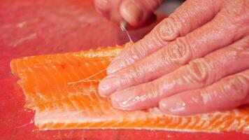 Hand cutting salmon on red board in closeup gesture video