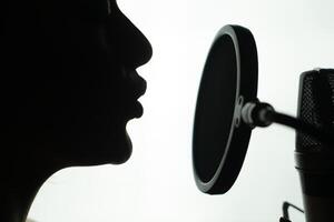 Black and white profile of a young woman singing at the round microphone. Close-up of female's face near the mic. photo