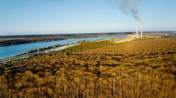 aéreo ver de el bosque en temprano primavera, azul río y campos debajo el claro cielo. natural antecedentes y un fábrica con fumar cuales viene fuera desde el tubería foto