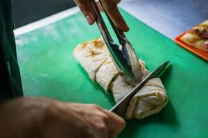 cook cuts a pancake roll with a knife on the board for serving a dish. photo