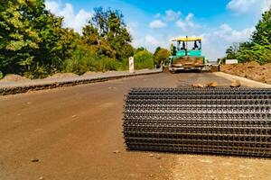 roll of reinforced mesh lays on the road on the background of professional equipment for the repair of roads. Close-up photo