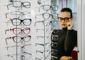 Stand with glasses in an optician's store with a beautiful girl in the background. Eyeglasses shop. Ophthalmology. photo