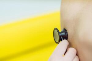 Child is examined by a doctor with a stethoscope on blurred background. The doctor listens to the lungs and heart with a stethoscope. Close-up photo