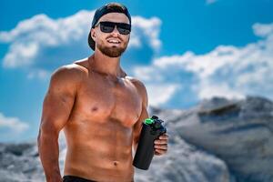 Portrait of a handsome halfnacked bodybuilder man on a mountain with a bottle of water. photo