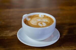 white cup with latte stands on the table in the cafe. The original pattern in the cup with latte. Close-up photo