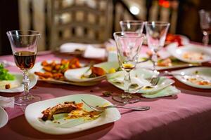 Plates with crumbs of food and glasses for wine on the table with pink tablecloth in the restaurant. Remains of food in plates after lunch or dinner. photo