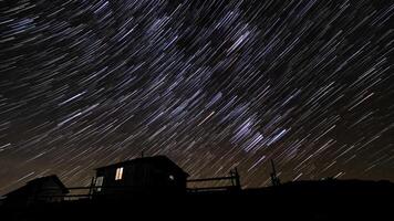 tid upphöra av kometformad stjärna spår över trä- hus i de natt himmel. stjärnor flytta runt om en polär stjärna. 4k video