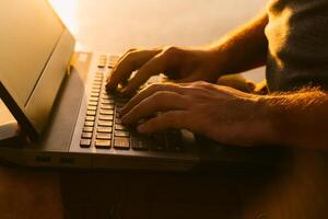 Mans' hands work on the laptop in the riverside at sunset. Business man typing modern laptop against beautiful summer landscape in the evening. Close up photo