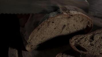 Cutting slice of homemade Crusty rye bread with a sharp knife on wooden board, closeup slow motion video