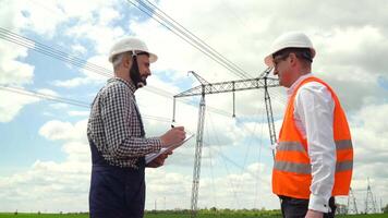 dos ingenieros trabajando cerca transmisión líneas. gerente da tarea a subordinar cerca transmisión líneas. electricidad pilones video