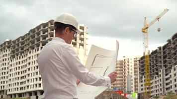 Male builder engineer architect in hard hat reading blueprint on construction site video