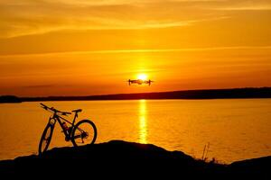 silueta de un bicicleta a puesta de sol. zumbido quadcopter con digital cámara volador a puesta de sol foto