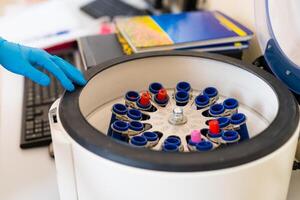 The laboratory assistant places a test tube with a sample for analysis into a centrifuge apparatus, close-up photo